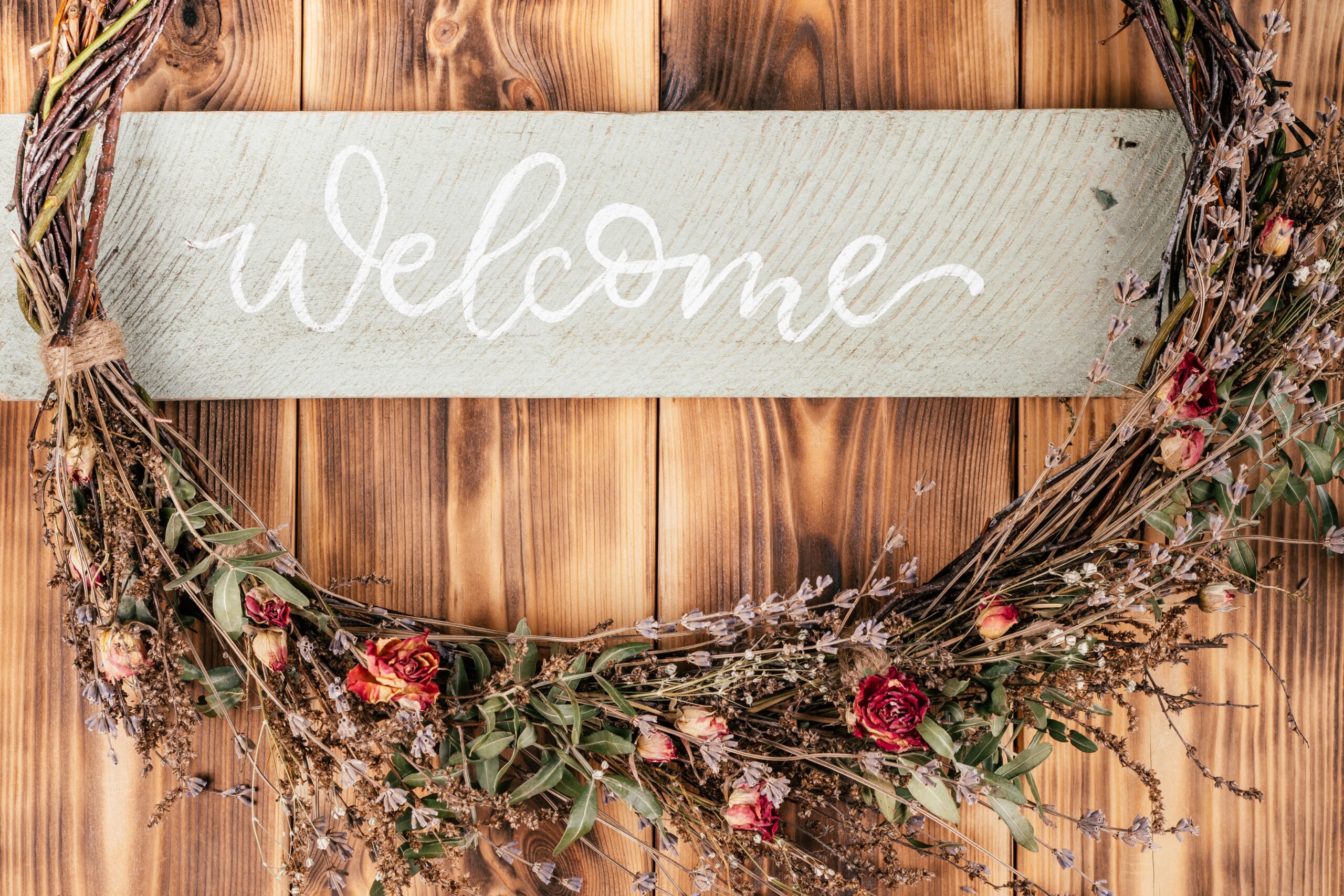 Dried flower, crafting tightly woven wreath with string and name board welcome. Rustic brown wooden and planking door on background. Celebration, preparation, warm greeting of guests. No people